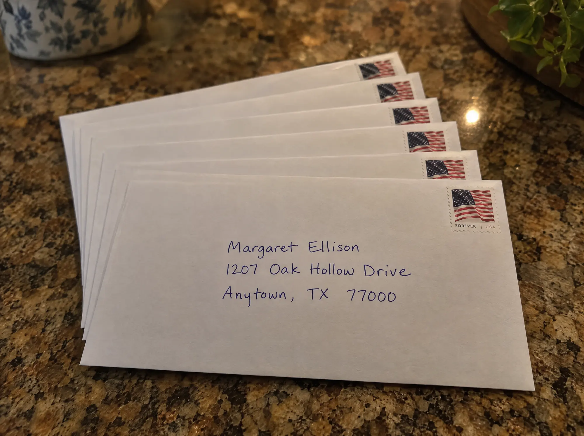 A fanned stack of hand addressed white envelopes, each with a Forever flag stamp